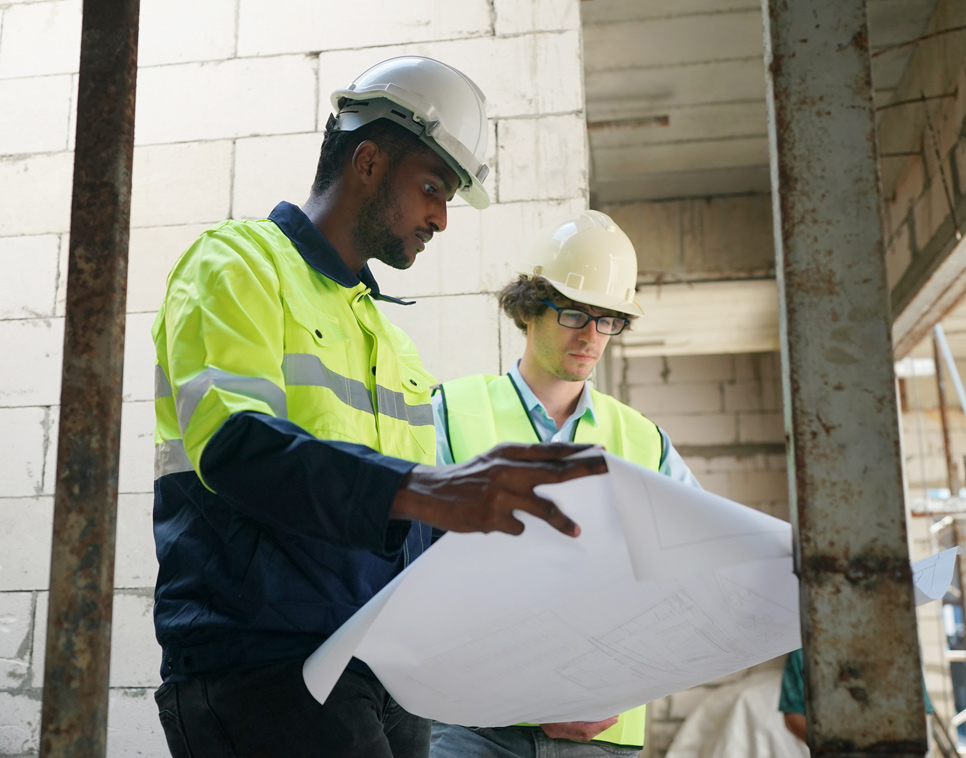 Construction workers wearing neon vests and hard hats reviewing blueprints