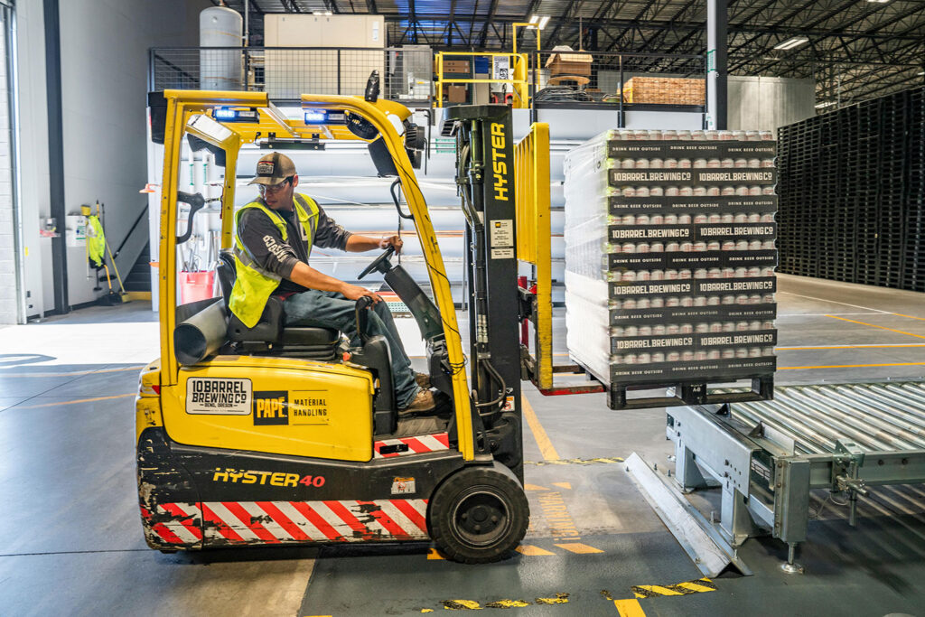 Man operating forklift with cases of beer in a storage warehouse