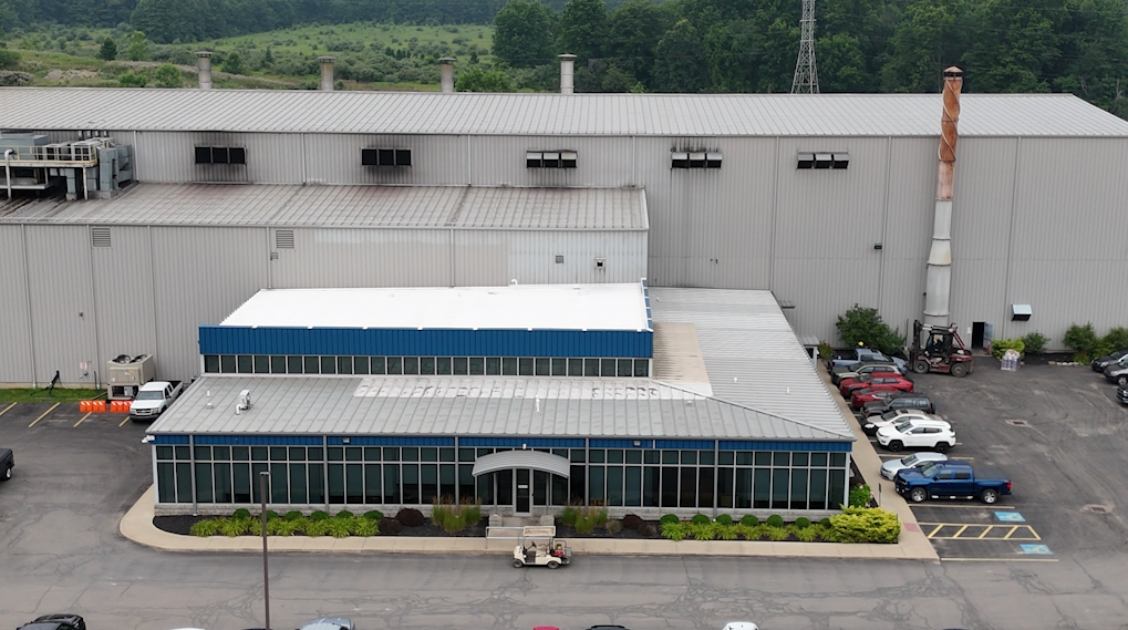 Industrial warehouse with windows, parking lot with cars, and landscaping bushes