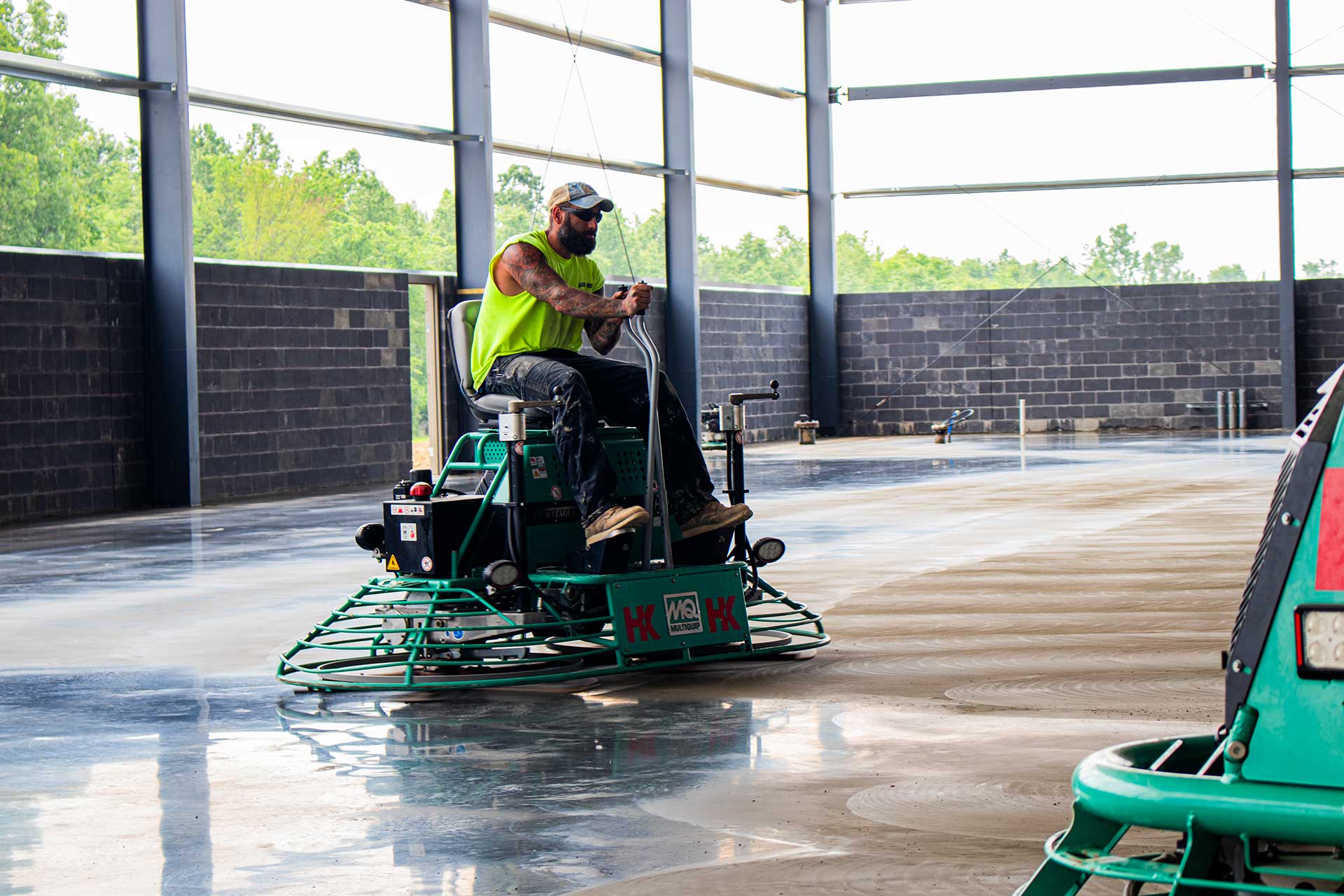 Man wearing neon cutoff shirt, jeans, and booths operating floor cleaning machine